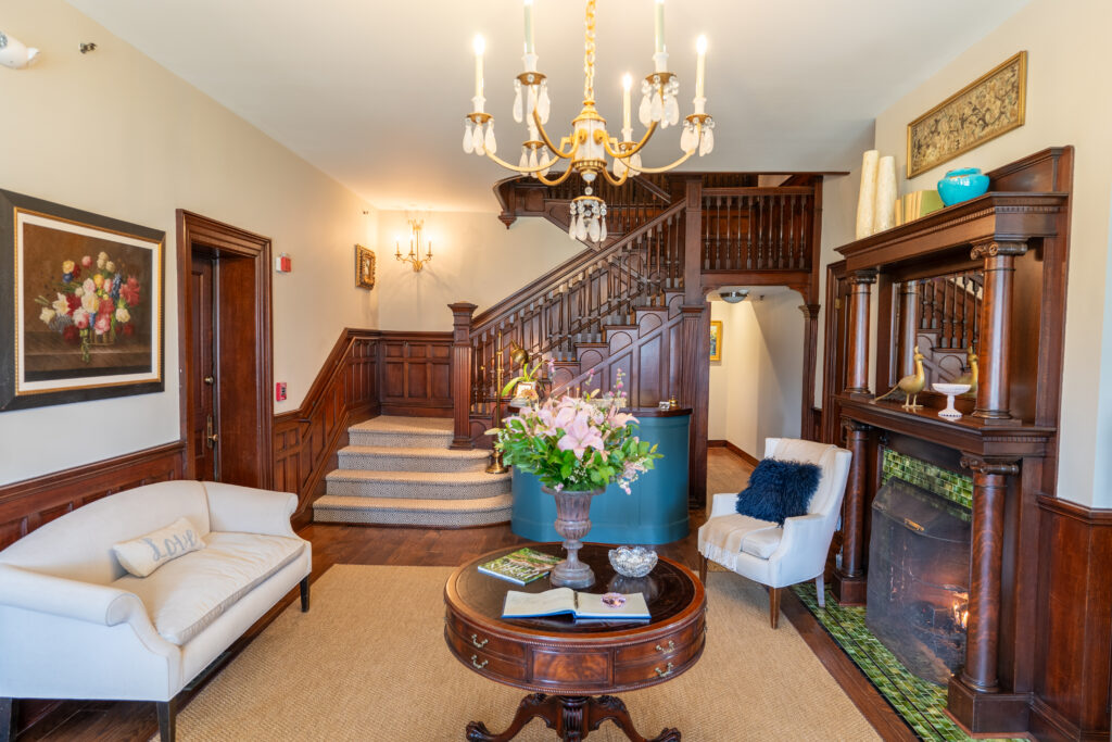 West Lane Inn lobby with grand staircase, chandelier, fireplace, and fresh floral arrangement